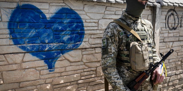 A Ukrainian soldier poses for a photo in front of a wall of heart graffiti during his patrol in an undisclosed location in Kharkiv oblast.