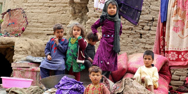 In this photo taken on May 4, 2022, flash flood-affected children sit outside their damaged house at Qadis district in Badghis province. - Flash floods and storms killed at least 18 people after ravaging several provinces of Afghanistan.