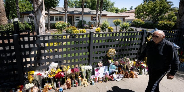 Pedestrians pass by a growing memorial in front of the home in the 22500 block of Victory Boulevard Wednesday, May 11, 2022. The home is where three children were allegedly killed by their mother.