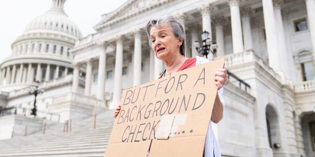 Marnie Beale of Arlington, Va., holds a sign at the Senate steps of the U.S. Capitol calling for background checks on gun purchases on Wednesday, May 25, 2022, after the latest mass shooting at a Texas elementary school