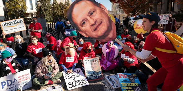  An activist with The Center for Popular Democracy Action holds a photo of U.S. Supreme Court justice Samuel Alito as they block an intersection during a demonstration in front of the U.S. Supreme Court on December 01, 2021 in Washington, DC. 