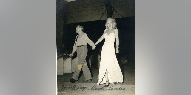 Carole Landis in white floor-length gown holding the hand of Jack Benny.