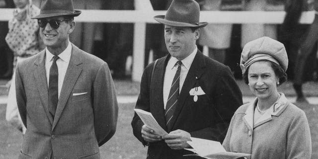 La reine Elizabeth II et le duc d'Édimbourg, à gauche, discutent avec le directeur de course Lord Porchester aux courses de Newbury, en Angleterre, le 30 septembre 1969.