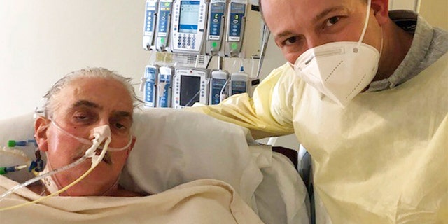 FILE: David Bennett Jr., right, stands next to his father's hospital bed in Baltimore, Md., on Jan. 12, 2022, five days after doctors transplanted a pig heart into Bennett Sr., in a last-ditch effort to save his life. 