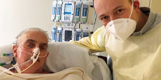FILE: David Bennett Jr., right, stands next to his father's hospital bed in Baltimore, Md., on Jan. 12, 2022, five days after doctors transplanted a pig heart into Bennett Sr., in a last-ditch effort to save his life.