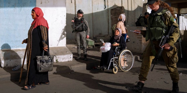 Palestinian women walk past a section of the Israeli separation barrier on their way to pray at Al Aqsa Mosque in Jerusalem on April 29, 2022.