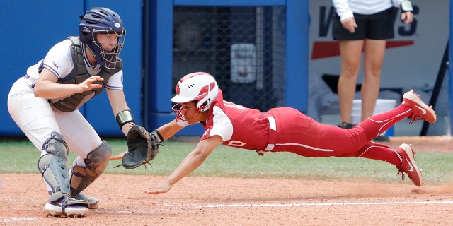 Oklahoma's Rylie Boone (0) slides in at home past James Madison catcher Lauren Bernett (22) to score a run in the sixth inning during a Women's College World Series semi finals game at USA Softball Hall of Fame Stadium. Oklahoma won 6-3.