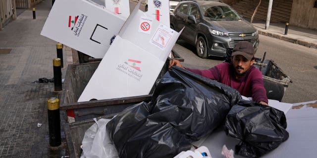 A man searches in trash dumpsters for recyclable items to resell next to cardboard voting booths that were used Sunday in the Lebanese parliamentary elections in Beirut, Lebanon, Monday, May 16, 2022.