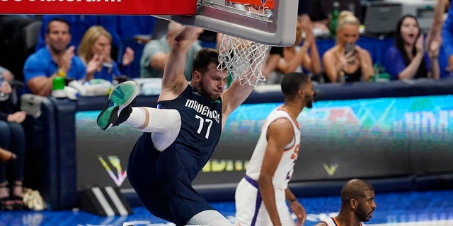 Dallas Mavericks guard Luka Doncic (77) hangs on the rim over Phoenix Suns guard Chris Paul, right, after scoring during the second half of Game 6 of an NBA basketball second-round playoff series, Thursday, May 12, 2022, in Dallas.