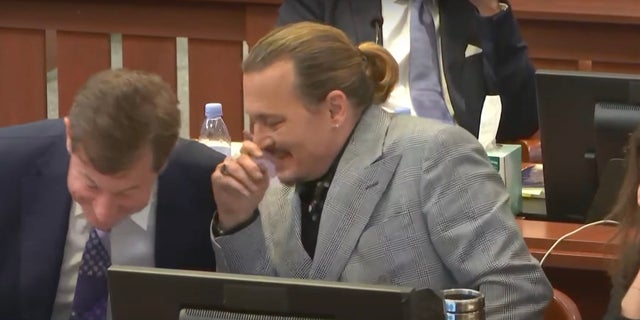 A screenshot of Johnny Depp laughing and chatting with his lawyer, Ben Chew, while Ellen Barkin's pre-recorded deposition was played for jurors at his defamation trial against Amber Heard. 