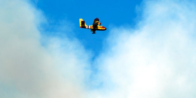 A firefighting plane flies in front of a plume of smoke near Las Vegas, N.M., on Tuesday, May 3, 2022.