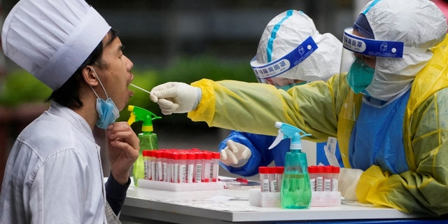 A medical worker in a protective suit collects a swab sample from a chef for nucleic acid testing, during lockdown, amid the coronavirus disease (COVID-19) pandemic, in Shanghai, China, May 13, 2022. 