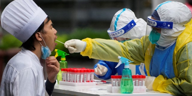 A medical worker in a protective suit collects a swab sample from a chef for nucleic acid testing, during lockdown, amid the coronavirus disease (COVID-19) pandemic, in Shanghai, China, May 13, 2022.