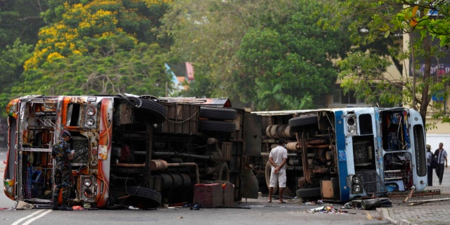 Sri Lankan government soldiers stand guard near burnt buses a day after clashes between government supporters and anti-government protesters in Colombo, Sri Lanka, Tuesday, May 10, 2022. 