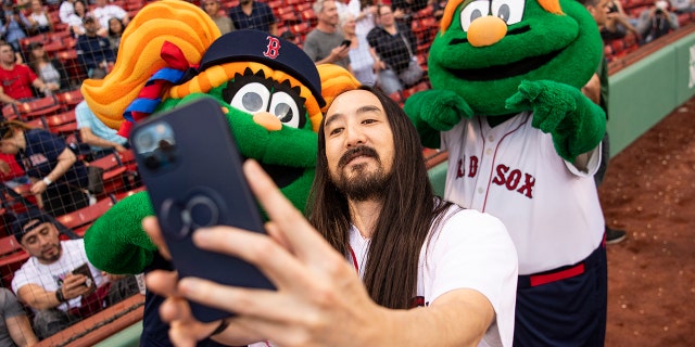 El DJ Steve Aoki posa para una selfie con las mascotas de los Medias Rojas, Tessie y Wally, antes de lanzar su primer espectáculo festivo el 16 de mayo de 2022 en Fenway Park.