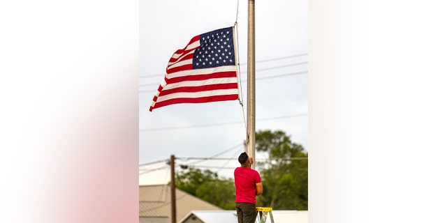 A man lowers the American flag to half staff at his Uvalde, Texas, hotel hours after a shooter entered Robb Elementary School in Uvalde and killed multiple children and adults. (William Luther/The San Antonio Express-News via AP)