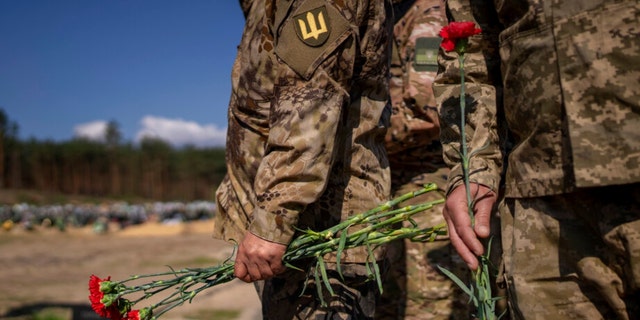 Irpin Territorial Defence and Ukrainian Army soldiers hold flowers to be placed on the graves of fallen comrades during the Russian occupation, at the cemetery of Irpin, 在基辅郊区, 在星期天, 可能 1, 2022. 