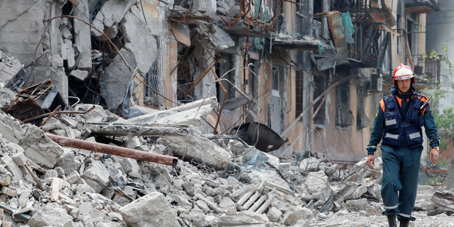 A member of the Russian Foreign Ministry walks near a destroyed residence in Mariupol, Ukraine, on Friday, May 11.