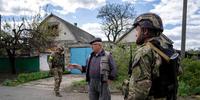 A Ukrainian serviceman talks with a local resident after de-mining the residential area after shelling of Russian forces in Maksymilyanivka, Ukraine, Tuesday, May 10, 2022. 