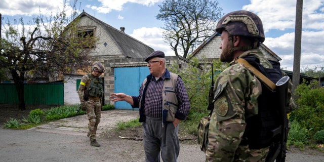 A Ukrainian serviceman talks with a local resident after de-mining the residential area after shelling of Russian forces in Maksymilyanivka, Ukraine, Tuesday, May 10, 2022. 