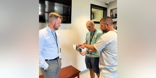 Air Traffic Manager Ryan Warren (links) and controller Robert Morgan (sentrum) show Harrison (far right) printouts of the Cessna 208 flight deck that was used to help him land the plane safely.