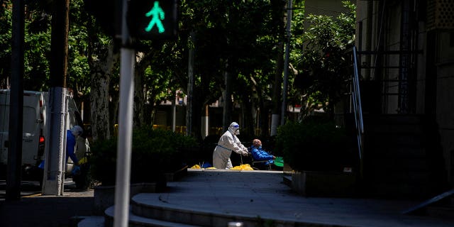 A worker in a protective suit helps a man in a wheelchair during lockdown amid the COVID-19 pandemic in Shanghai, China, May 5, 2022.