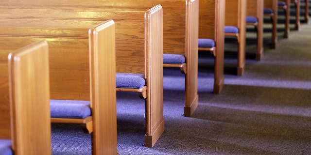 FILE- Window light is shining on rows of empty church pews in an empty church sanctuary.