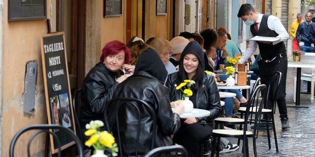 People gather at a bar in Rome, Sunday, May 1, 2022. Face masks, for the first time since the start of the pandemic, are no longer required in supermarkets, bars, restaurants, shops and most workplaces throughout Italy but remain mandatory on public transport, planes, trains and ships, theaters, cinemas, concert halls and for indoor sporting events. 