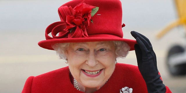 FILE - Britain's Queen Elizabeth II holds up her hat in strong winds as she arrives for a visit to RAF Valley, Anglesey, Wales April 1, 2011.
