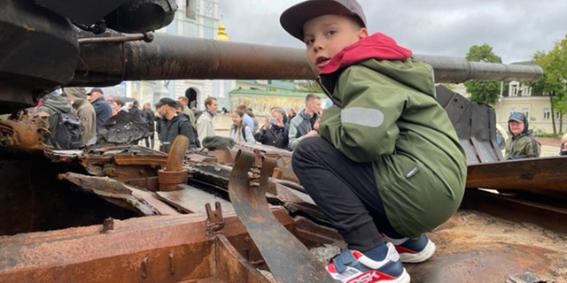 A Ukrainian boy stands atop a depleted Russian military tank in Lyiv. 
