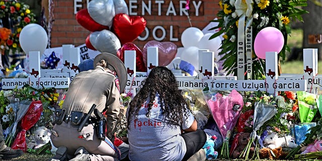 A police officer comforts family members at a memorial outside Robb Elementary in Uvalde.