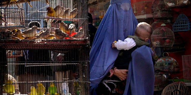 A woman wearing a burqa walks through a bird market holding her baby on Sunday, May 8, 2022, in the center of Kabul, Afghanistan.