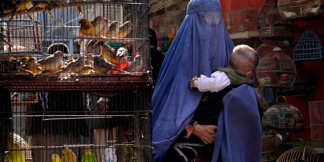 A woman wearing a burqa walks through a bird market as she holds her child, in downtown Kabul, Afghanistan, Sunday, May 8, 2022.