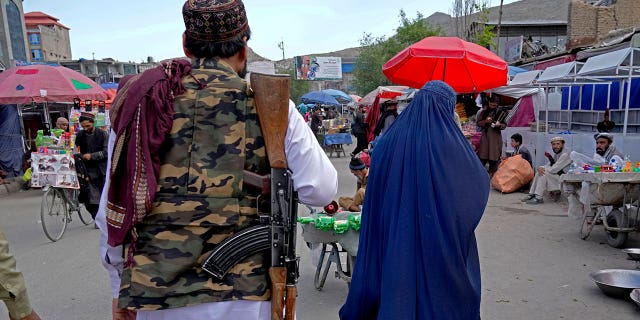 A woman wearing a burqa walks through the old market as a Taliban fighter stands guard, in downtown Kabul, Afghanistan, Sunday, May 8, 2022.