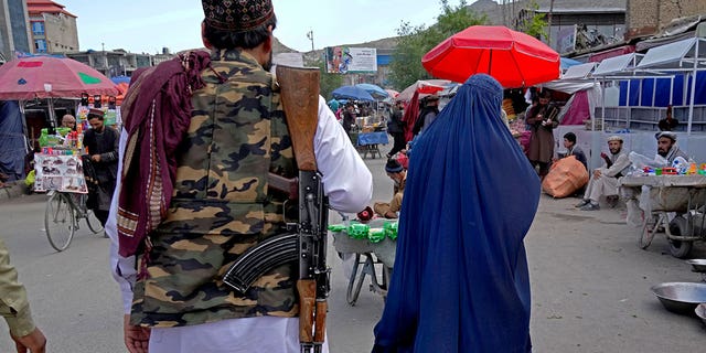 A woman wearing a burka walks through the old market as a Taliban fighter stands guard, in downtown Kabul, Afghanistan, May 8, 2022.