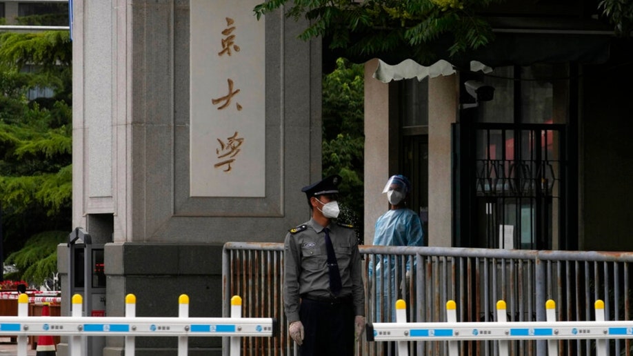 A security guard and a COVID-19 pandemic worker stand near an entrance to the Wanliu Campus of Beijing's Peking University
