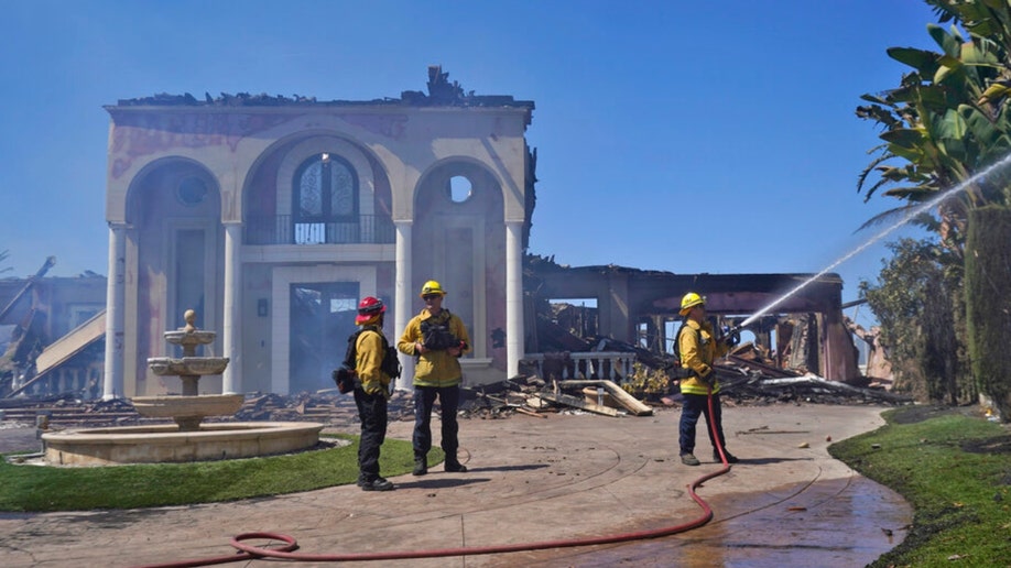 Firefighters protect the remains of a home damaged in California's Coastal Fire
