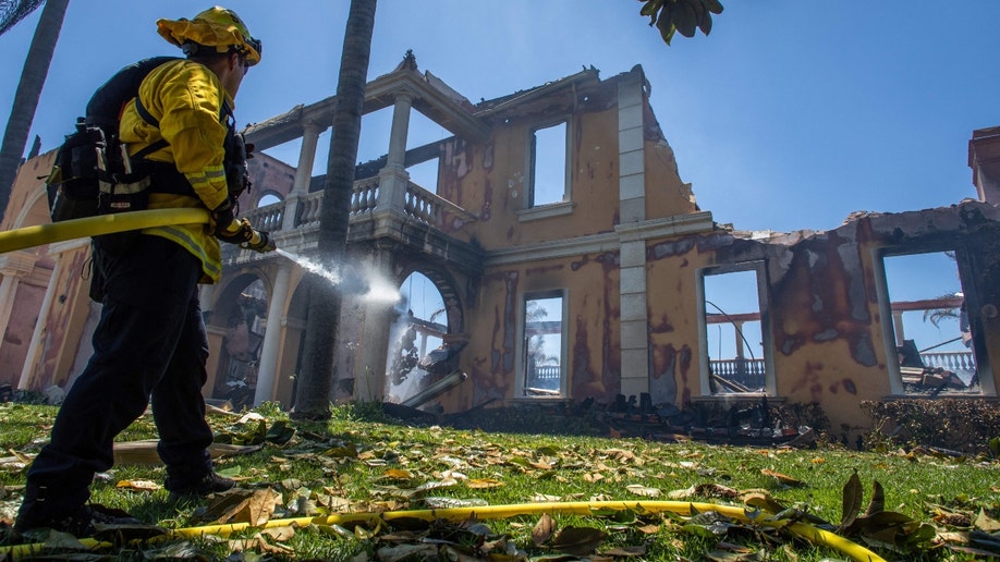 A firefighter uses a hose to put out hot spots in California's Coastal Fire