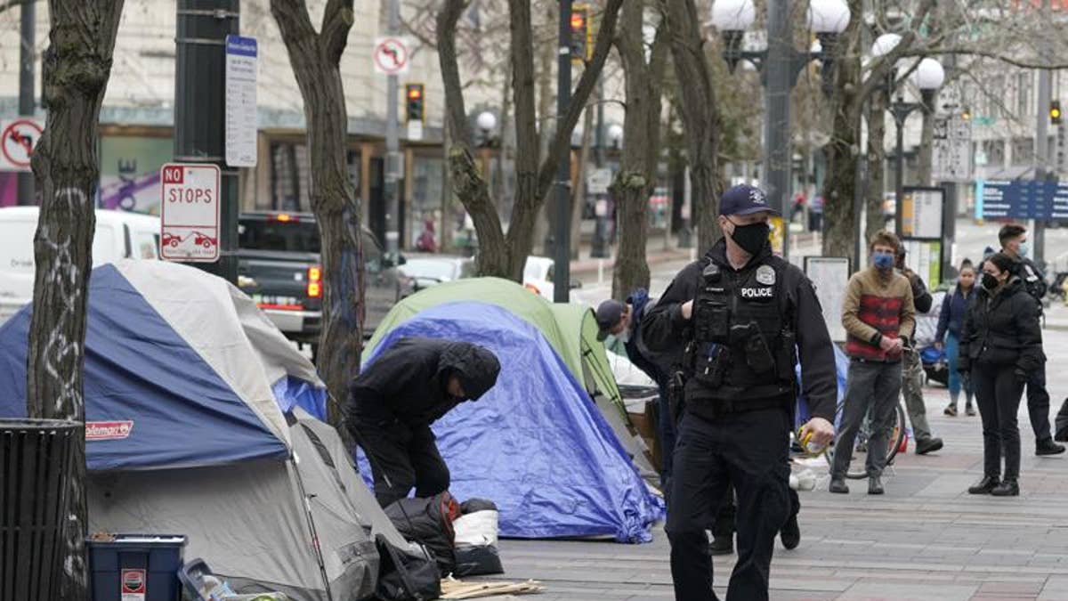 Police officer walking pass homeless encampment tents in Seattle