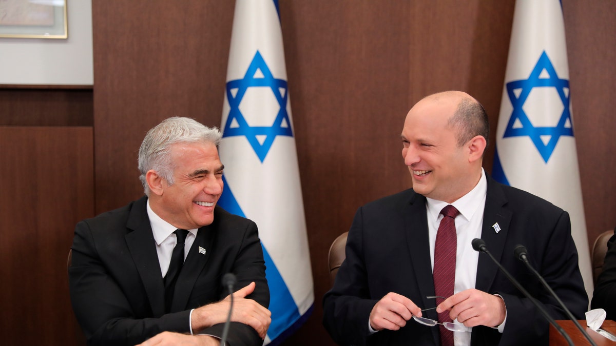 Naftali Bennett and Yair Lapid smiling in front of an Israeli flag