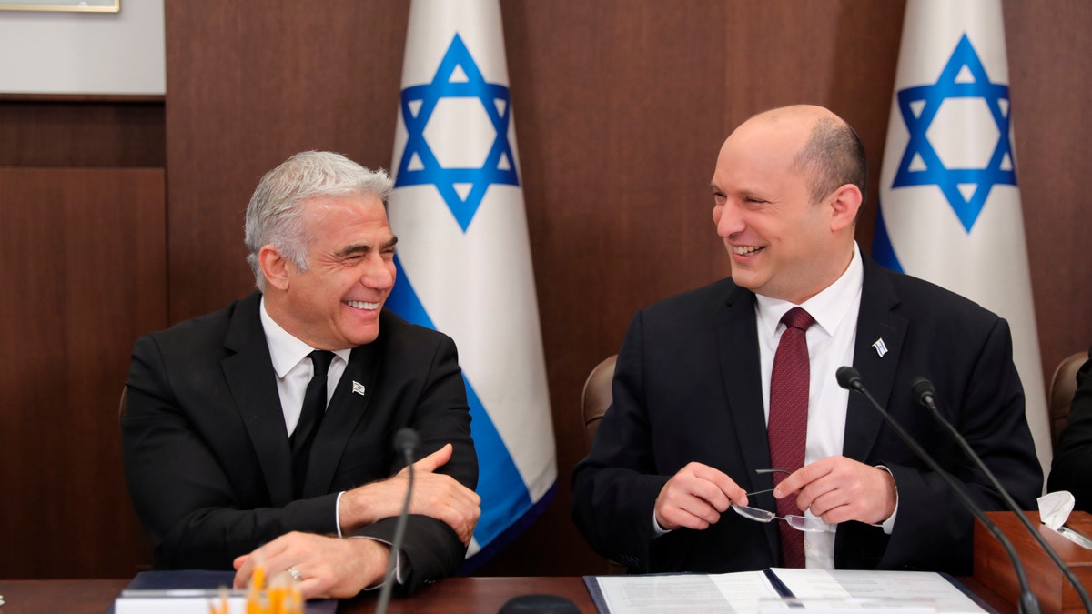 Naftali Bennett and Yair Lapid smiling in front of an Israeli flag