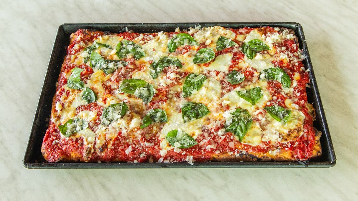 A roasting pan holds a pizza covered in tomato sauce, cheese and basil. 