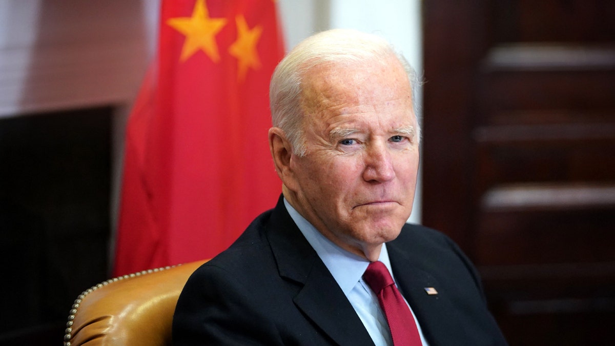 President Joe Biden in a suit looks on in front of a Chinese flag