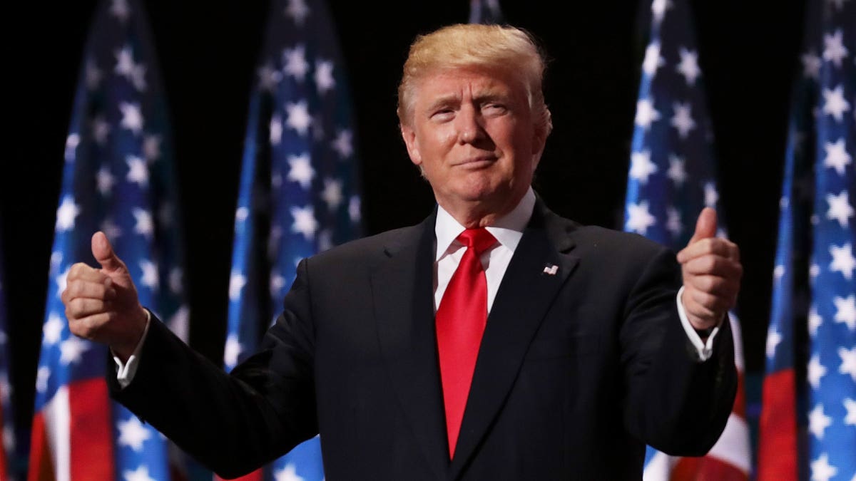 Wearing a suit and red tie, Donald Trump gives two thumbs up