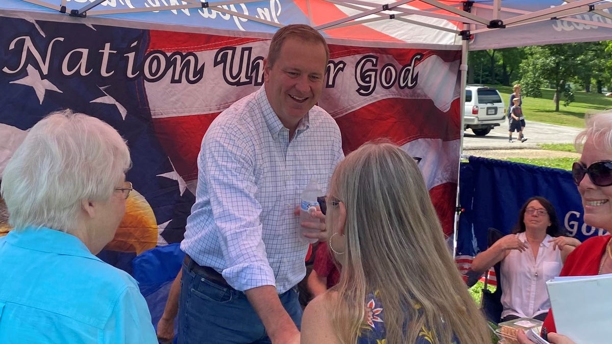 Missouri Attorney General Eric Schmitt shakes hands with voters in front of an American flag.