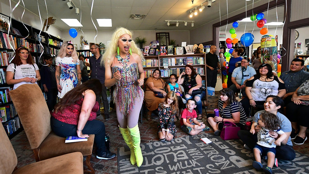 drag queen in elaborate makeup dances by children in library