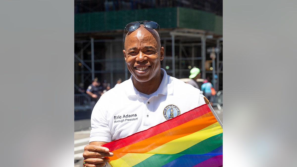 NYC Mayor Eric Adams smiles with rainbow pride flag