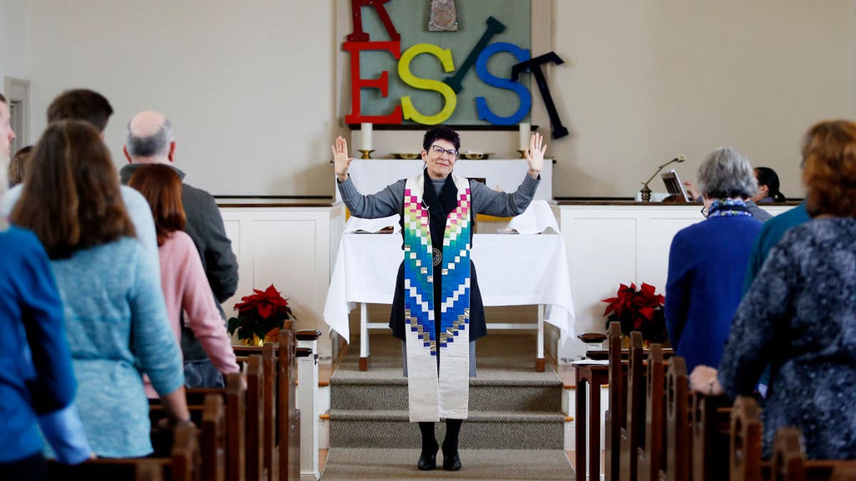 Woman pastor in front of church congregation with "resist" and cross in backgroundry United Methodist Church
