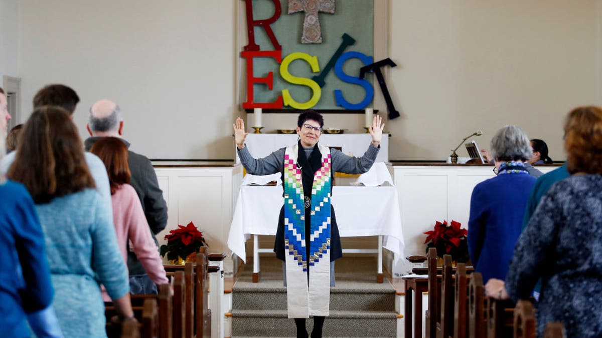 Woman pastor in front of church congregation with "resist" and cross in backgroundry United Methodist Church