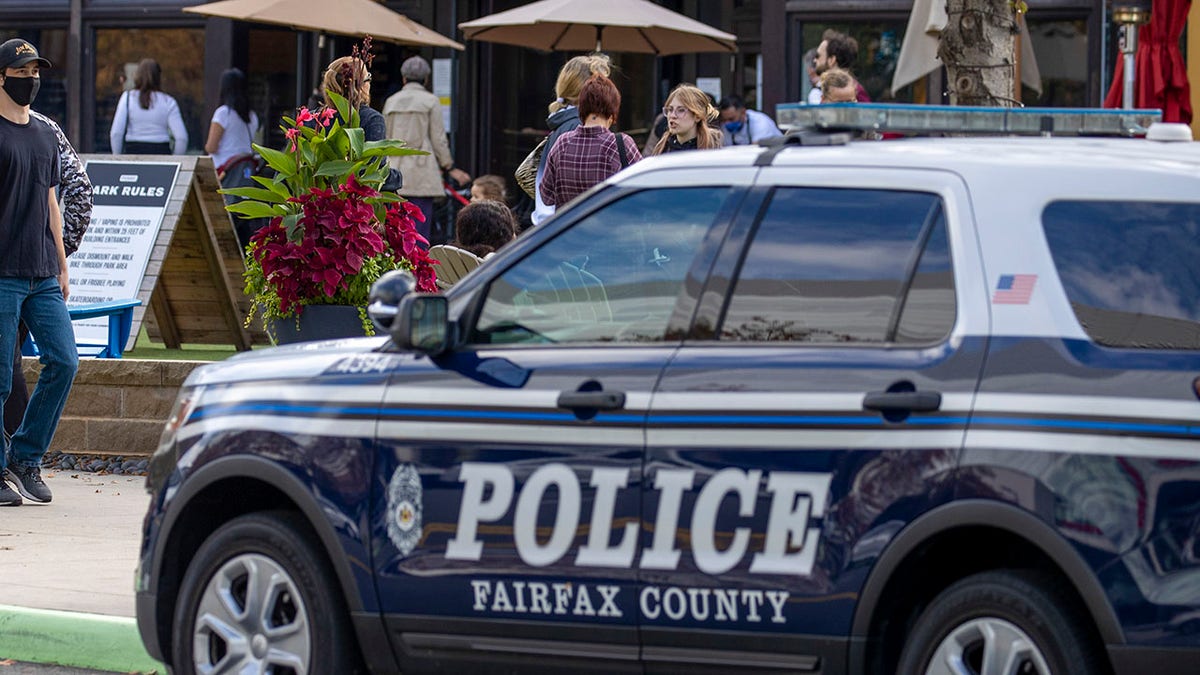 Fairfax County police vehicle on city street with people and restaurant in behind the vehicle.